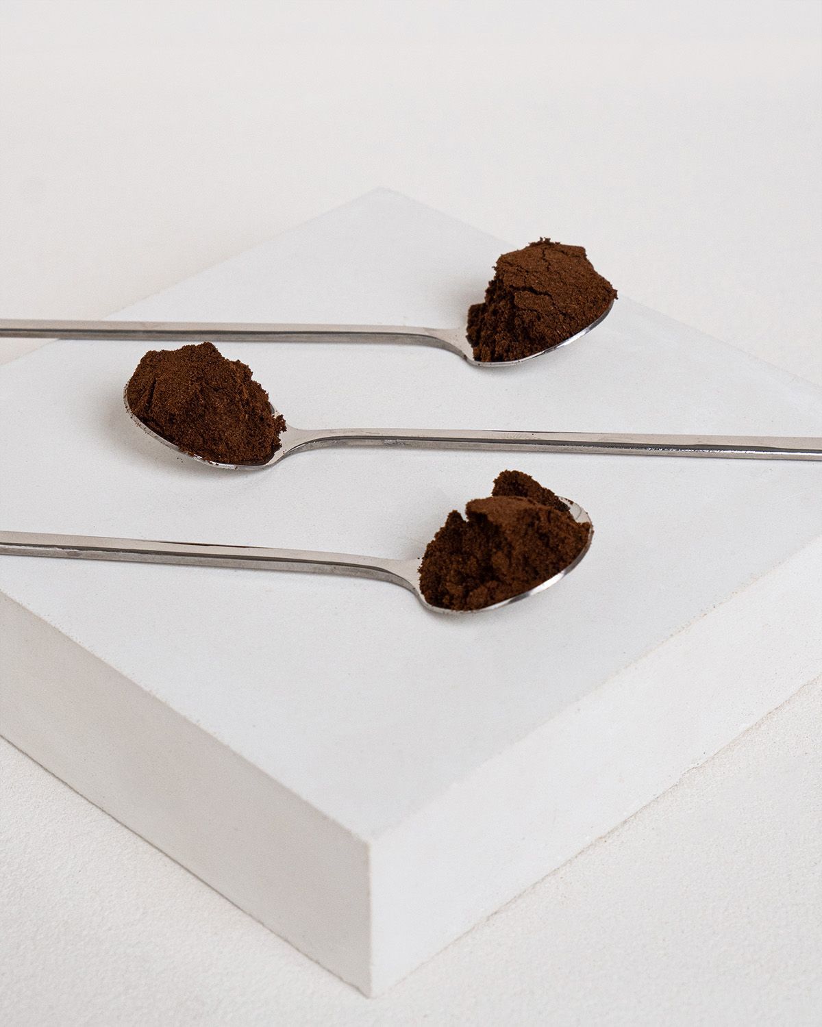 Drei Löffel mit gemahlenem Bourbon Vanillepulver auf einem weißen Podest.