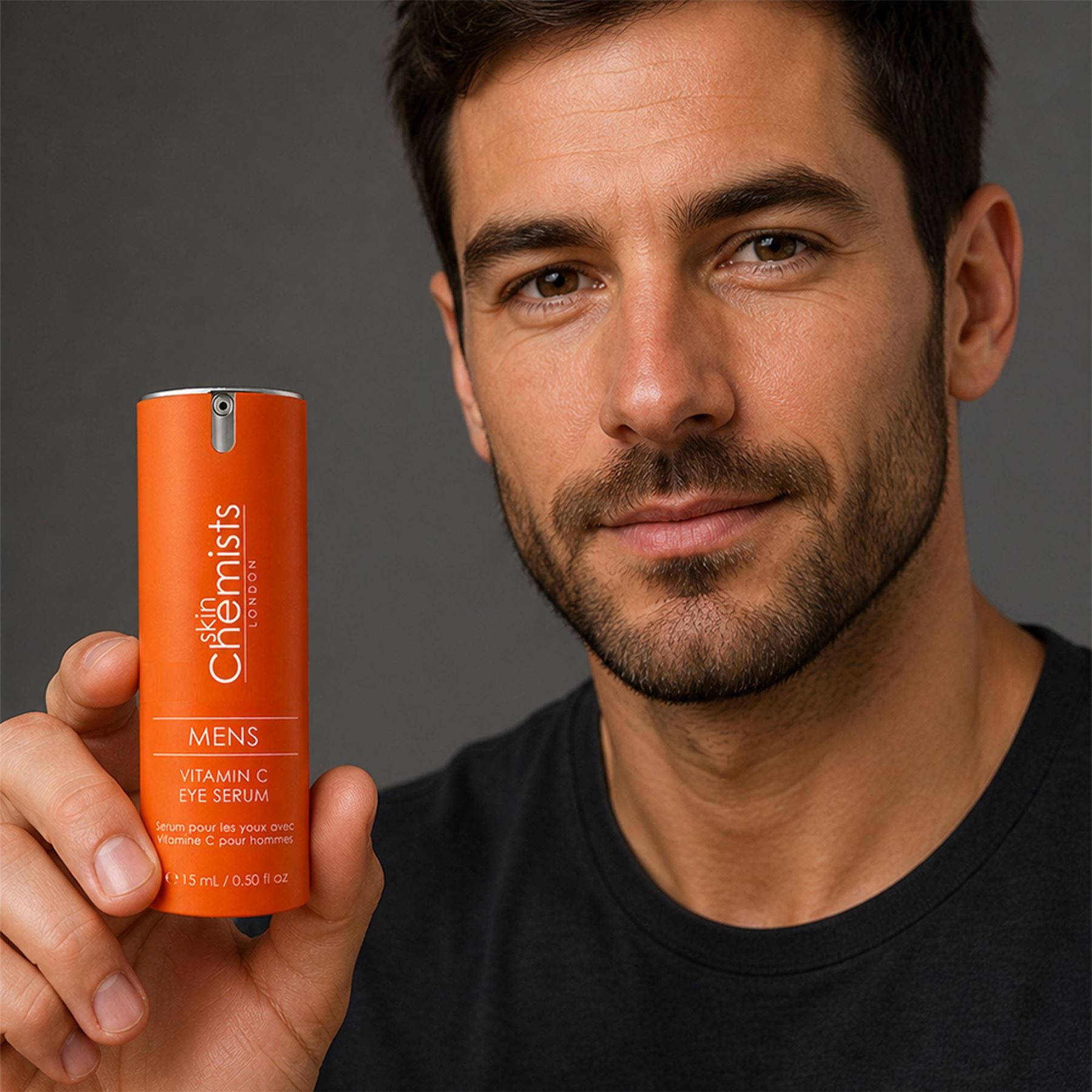Mann hält eine orangefarbene Flasche des SkinChemists Augenserums mit Vitamin C.