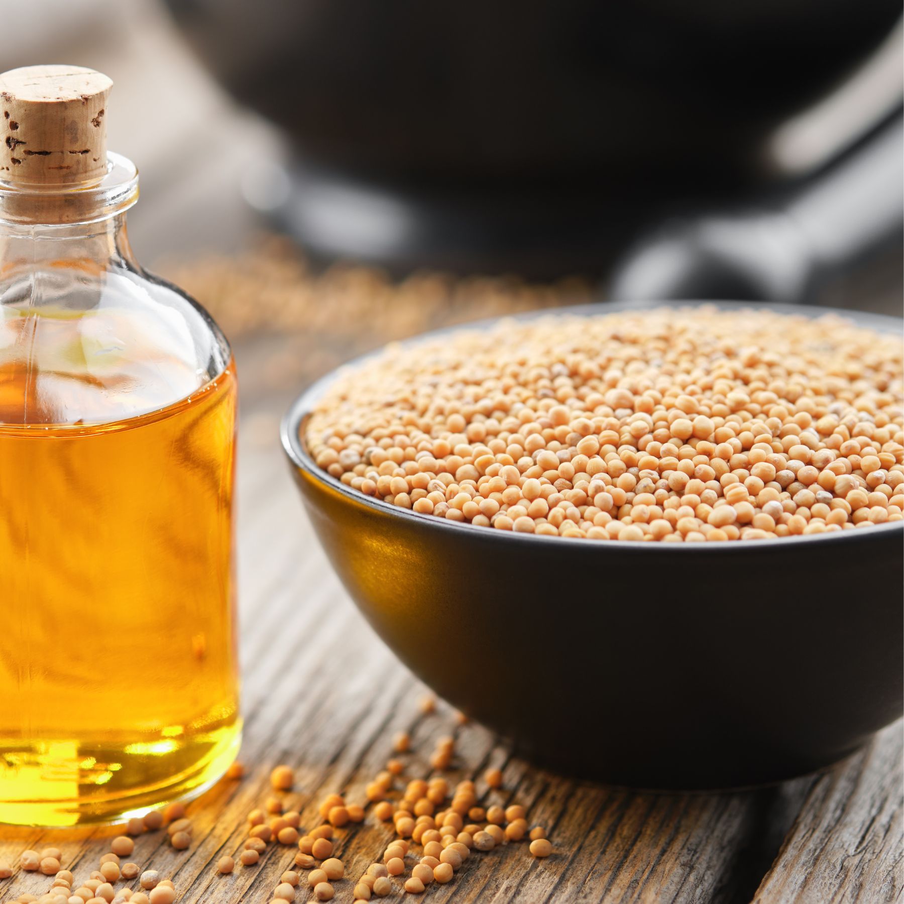 Glasflasche mit gelbem Öl und Korken neben einer Schüssel mit Senfkörnern. Auf Holzuntergrund.