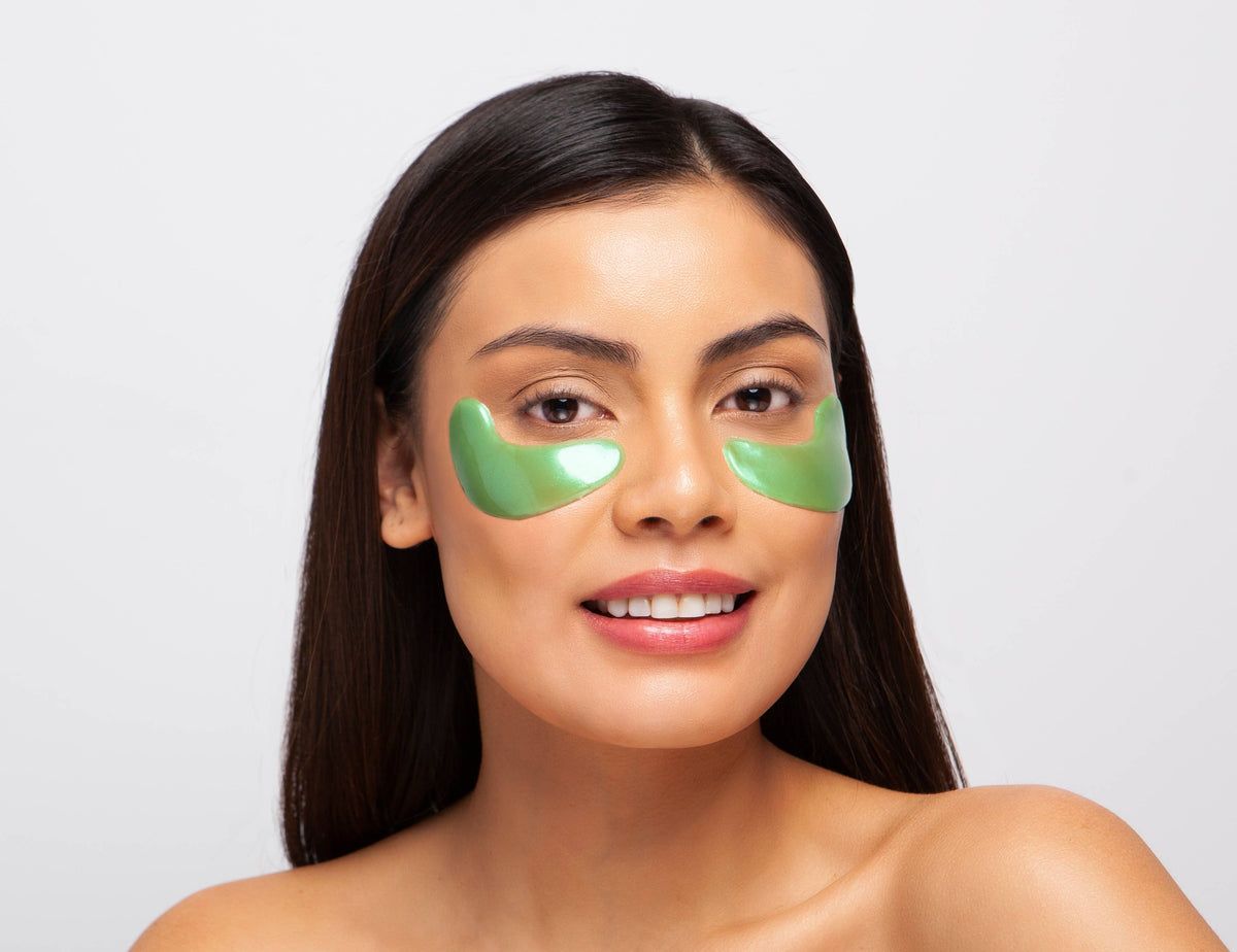 Frau mit grünen Hydrogel-Augenpads unter den Augen. Die Pads sind halbmondförmig.