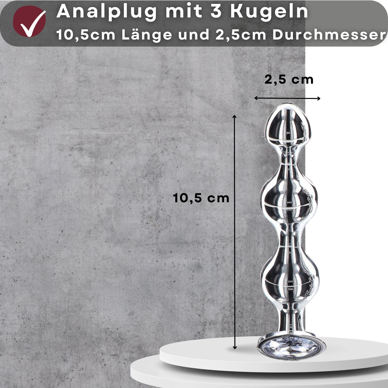 Analplug mit 3 Kugeln. 10,5 cm lang, 2,5 cm Durchmesser. Auf weißem Podest. Grauer Hintergrund.