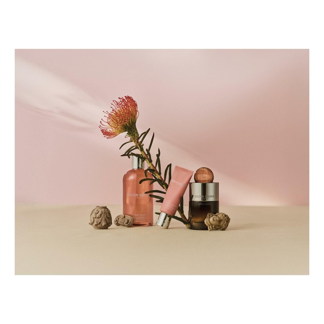 Produkt-Arrangement mit rosa Tube, Flasche und Flakon. Dekoration mit Blüte und Steinen. Hintergrund: rosa und beige.