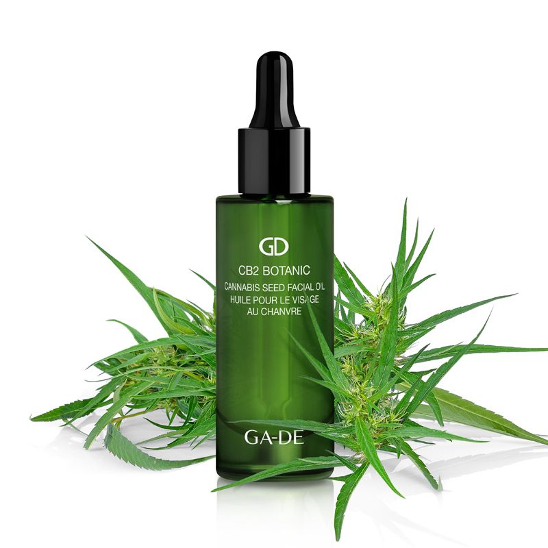 Grüne Glasflasche mit schwarzem Tropfer, umgeben von Cannabisblättern. Aufschrift: CB2 Botanic Cannabis Seed Facial Oil. Marke: GA-DE.