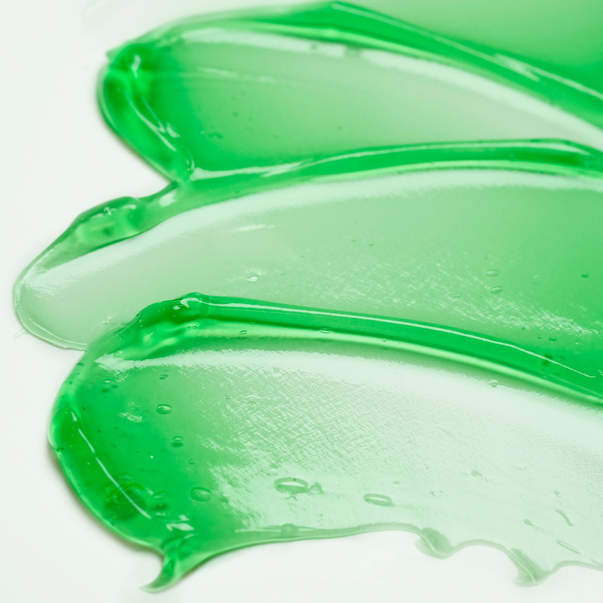 Grüne Gel-Schlieren auf weißem Hintergrund. Klare, transparente Textur. Einige Blasen sichtbar.