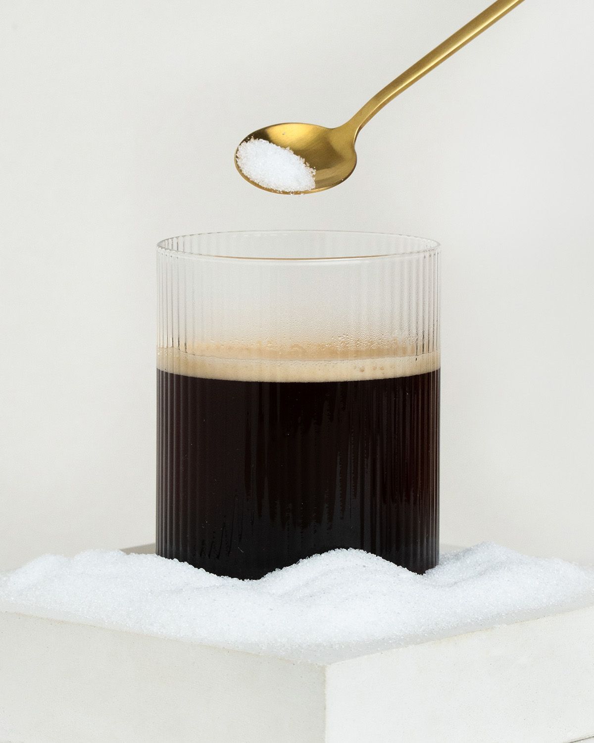 Ein Löffel mit Süßstoff über einem Glas Kaffee, umgeben von Süßstoffkristallen.