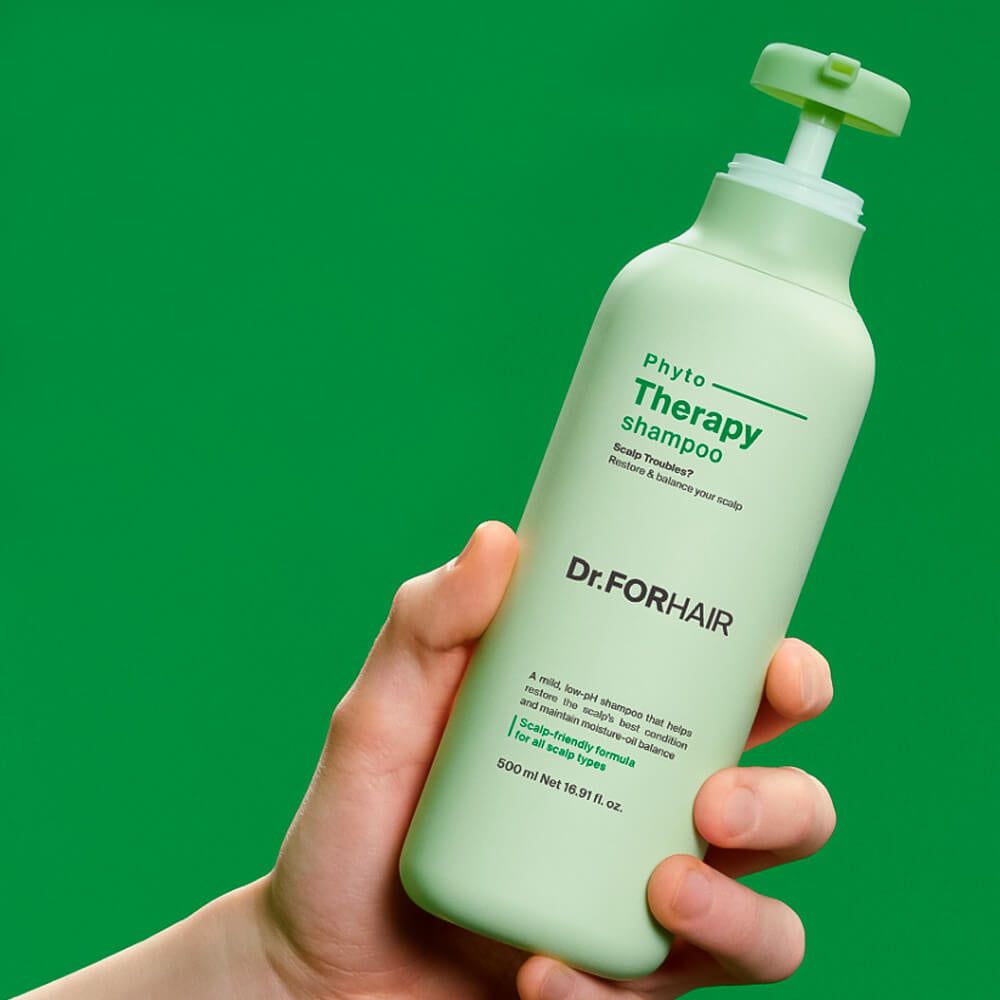Hand hält eine hellgrüne Flasche Dr. FORHAIR Phyto Therapy Shampoo mit grünem Hintergrund.