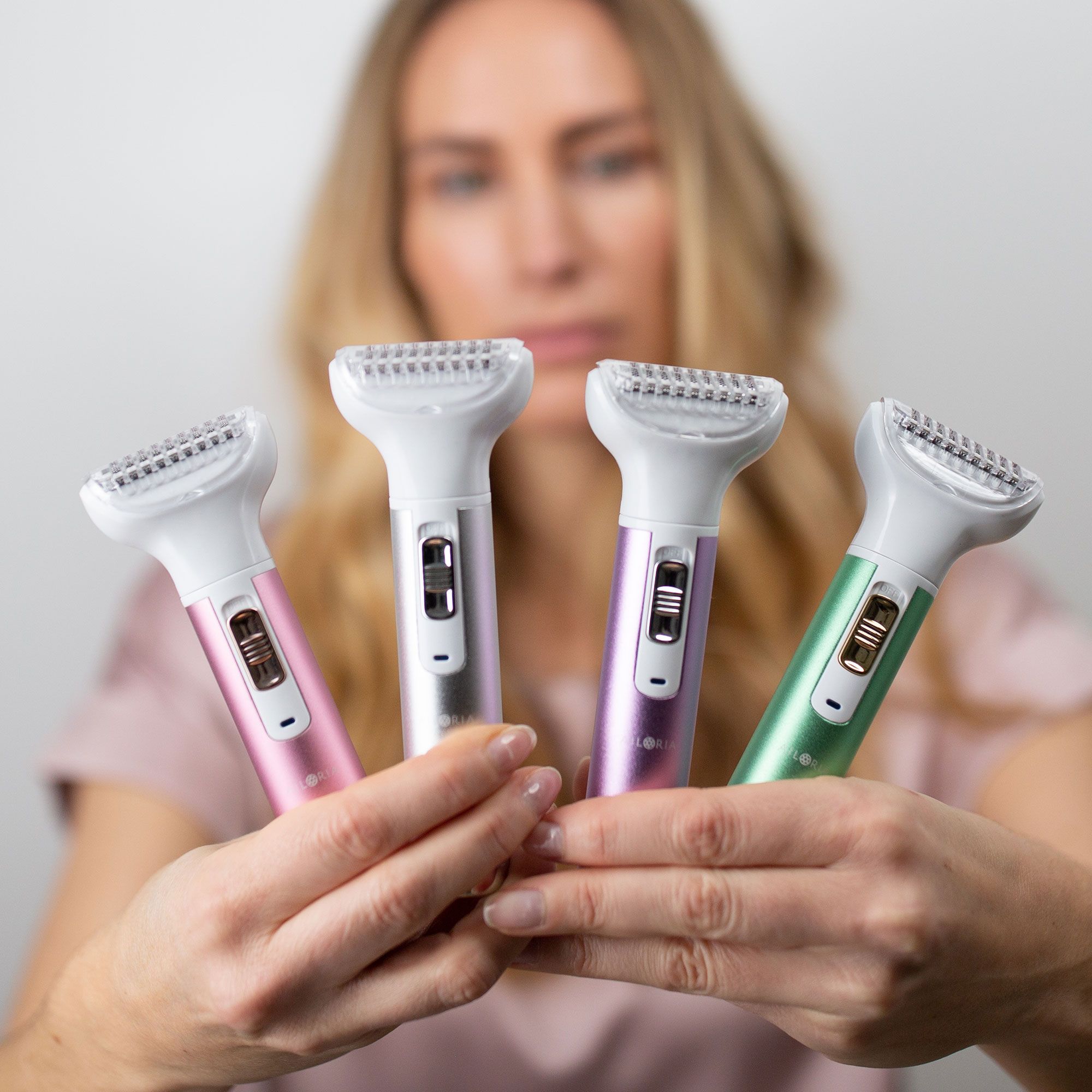 Vier Rasierer mit farbigen Griffen. Rosa, Silber, Lila und Grün. Frau hält die Rasierer in den Händen.