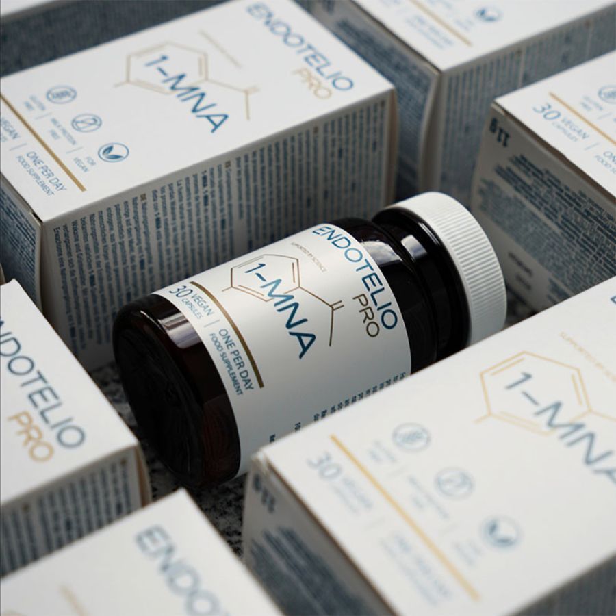 Braune Flasche mit Kapseln, umgeben von Schachteln. Aufschrift: Endotelio PRO, 1-MNA, 30 vegane Kapseln. Produktverpackung.