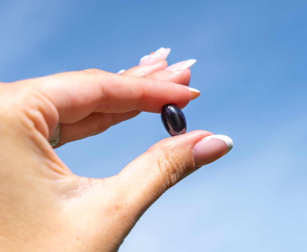 Eine Hand hält eine einzelne dunkelrote Aavalabs Astaxanthin Softgel-Kapsel.