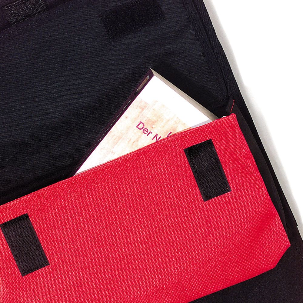 Schwarze Tasche mit rotem Akzent, teilweise geöffnet. Buch mit Titel "Der N..." sichtbar. Klettverschlüsse.
