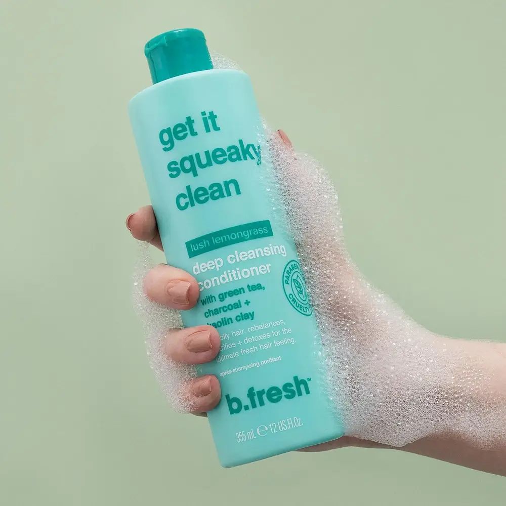 Türkisgrüne Flasche mit grünem Deckel. Aufschrift: Get it Squeaky Clean. In einer Hand gehalten, umgeben von Schaum.