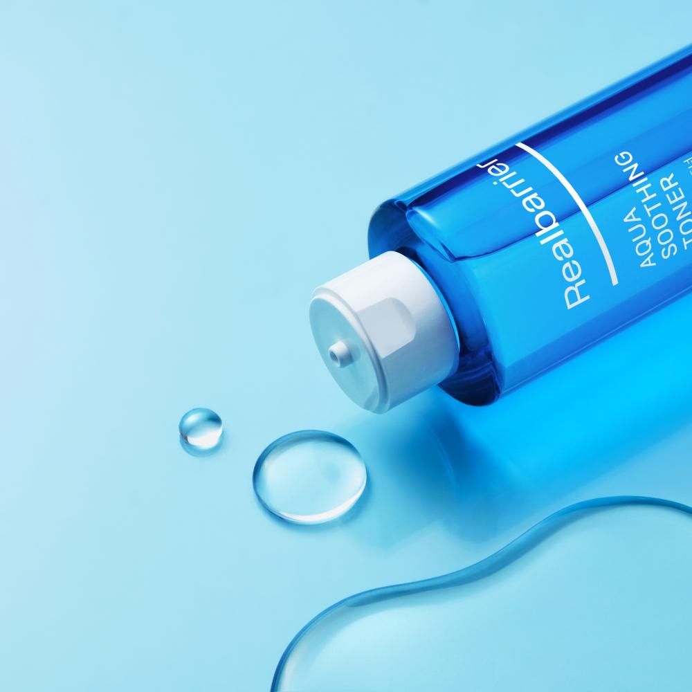 Blaues Toner-Fläschchen liegt. Daneben Wassertropfen. Aufschrift: Realbarrier, Aqua Soothing Toner. Weißer Deckel.