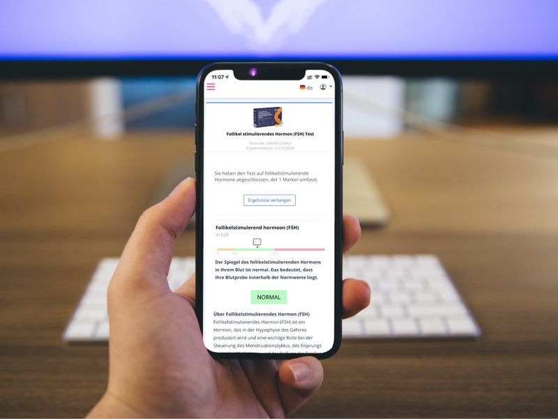 Smartphone mit Homed-IQ Testergebnis-Anzeige. Text in Deutsch. Hand hält Telefon vor Tastatur und Holzoberfläche.
