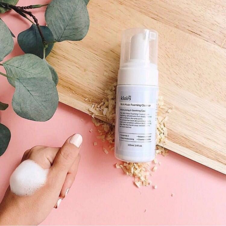 Weiße Flasche Klairs Rich Moist Foaming Cleanser auf Holzbrett. Schaum auf Hand. Rosa Hintergrund. Holz-Dekoration.