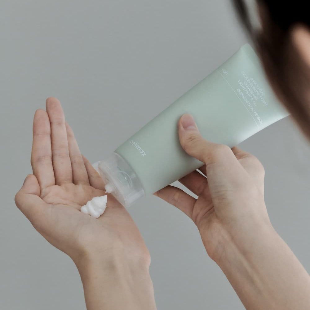 Eine Hand drückt Celimax Ji Woo Gae Cica BHA Akne-Reinigungsschaum in die andere Hand.