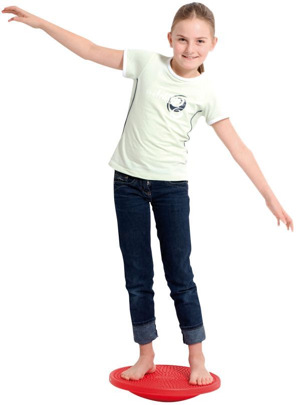 Mädchen balanciert auf rotem Kreisel, Arme seitlich. Helle Kleidung, Jeans.