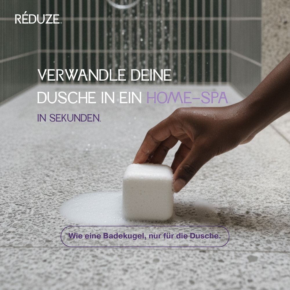 Hand legt einen weißen, quadratischen Duschwürfel auf eine Oberfläche. RÉDUZE ist sichtbar.