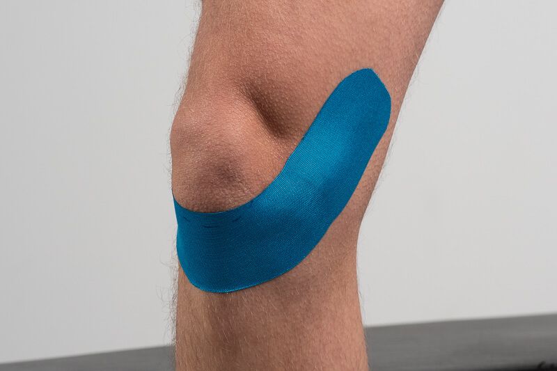 Blaues Kinesiotape auf einem Knie angebracht.