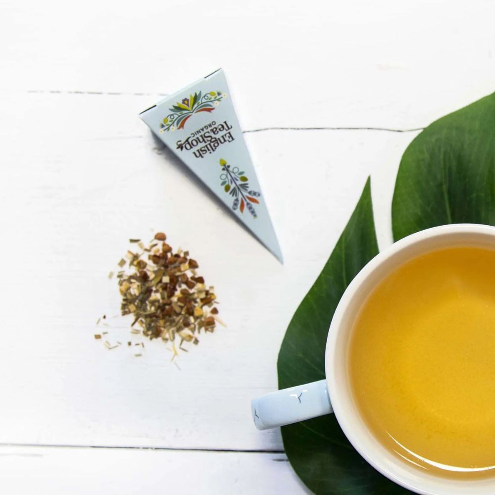 Teebeutel mit losen Blättern neben einer Tasse Tee. Pyramidenförmige Verpackung. Aufschrift: English Tea Shop Organic.