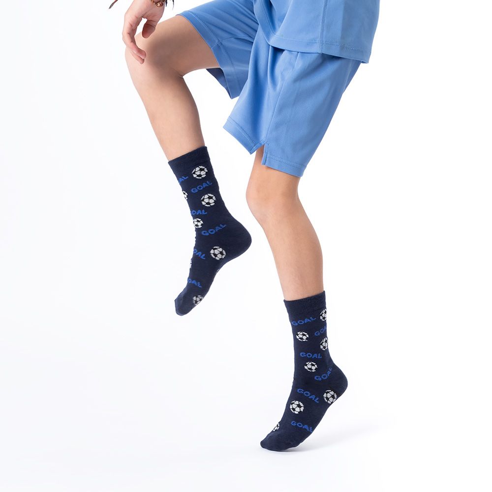 Junge steht, blaue Shorts. Blaue Socken mit Fußball- und Tor-Motiven. Hintergrund weiß.