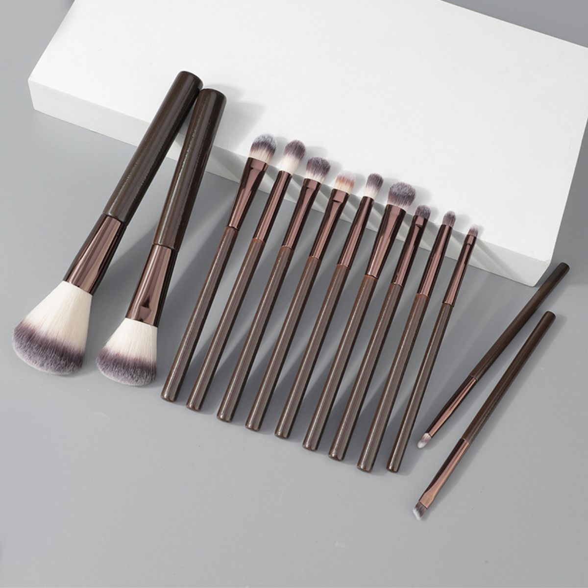 Ein Set aus 12 dunklen Make-up-Pinsel mit weißen und grauen Borsten.