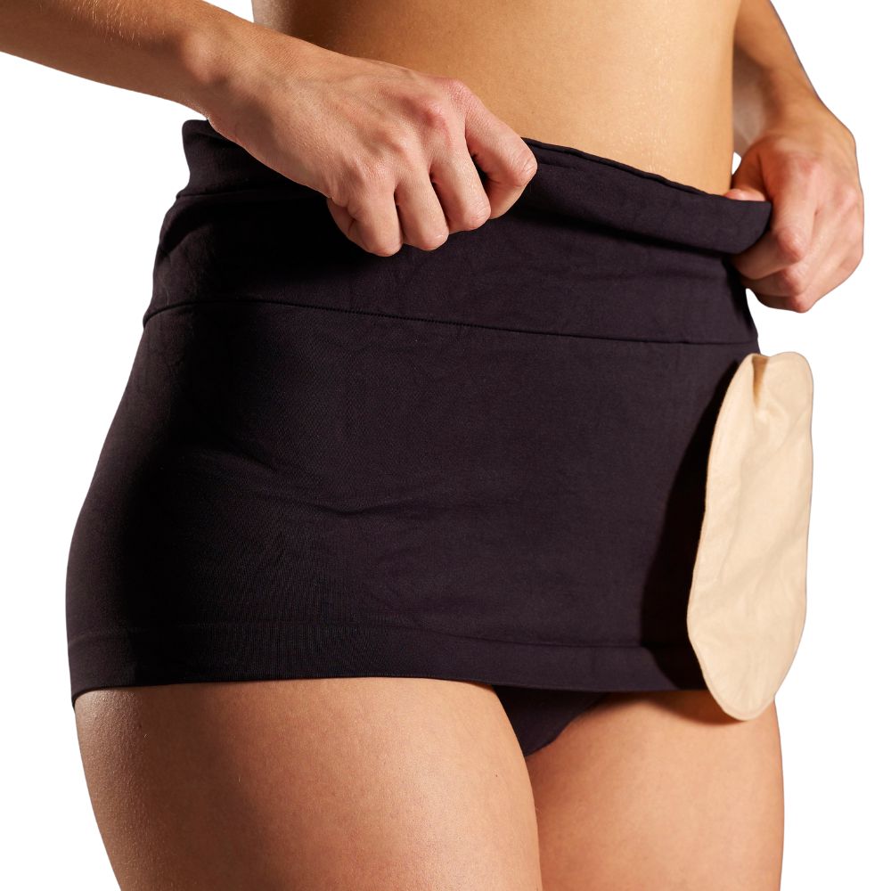 Schwarze Bauchbinde am Körper. Beige Stomabeutel sichtbar. Hände halten die Binde.