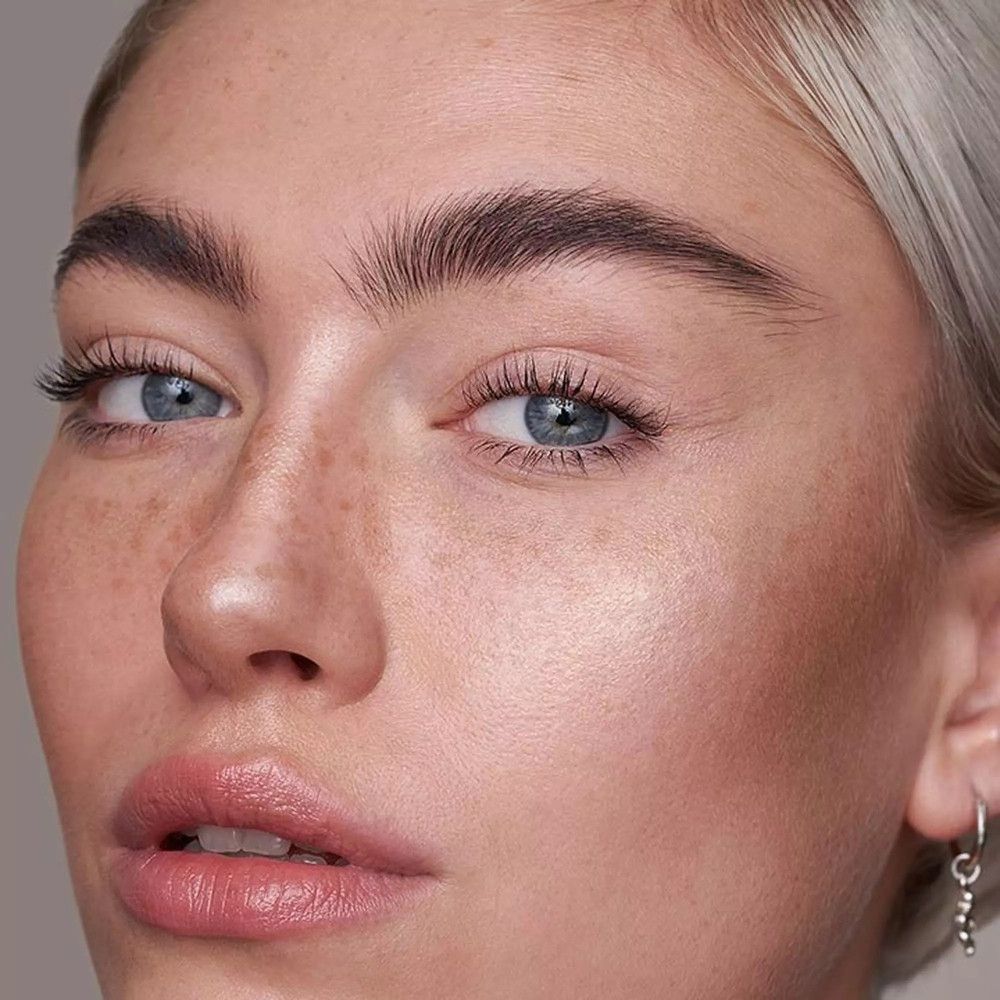 Nahaufnahme eines Gesichts mit glatter Haut und leichtem Make-up. Blaue Augen, helle Haut, rosafarbene Lippen.