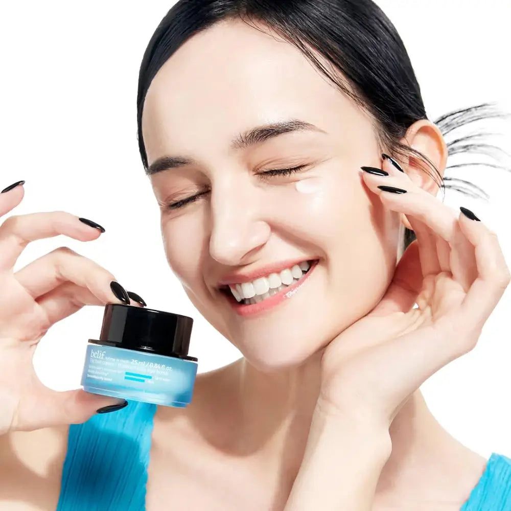 Frau hält ein blaues Tiegel mit schwarzem Deckel. Sie lächelt und hat Creme auf der Haut.