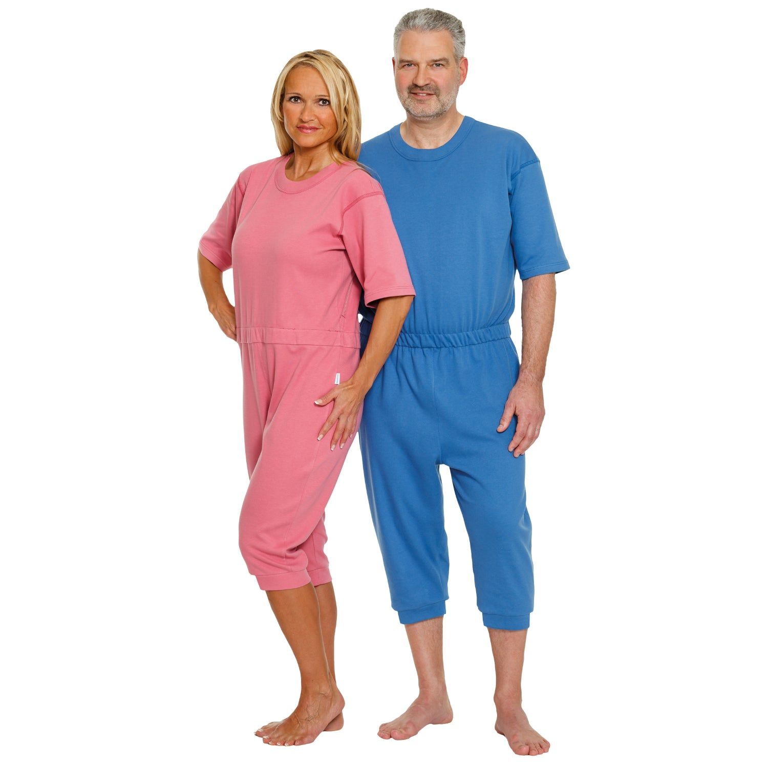 Zwei Personen tragen Pflegeoveralls. Eine Person in Rosa, die andere in Blau. Beide Overalls haben kurze Ärmel und Hosen.