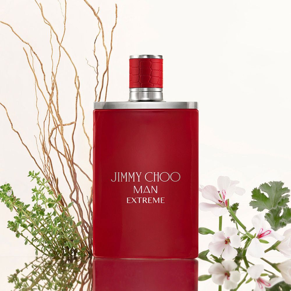 Rotes Parfümflakon. Aufschrift: JIMMY CHOO MAN EXTREME. Silberner Verschluss. Dekoration mit Pflanzen.