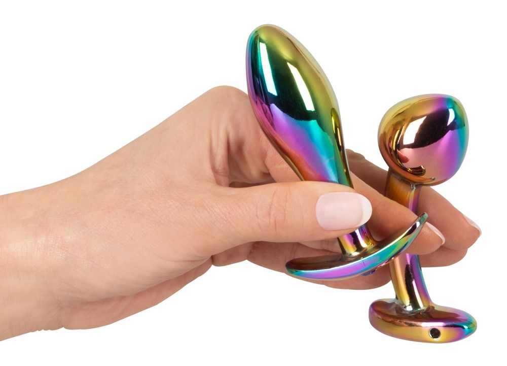 Hand hält zwei metallische Anal-Plugs in Regenbogenfarben.