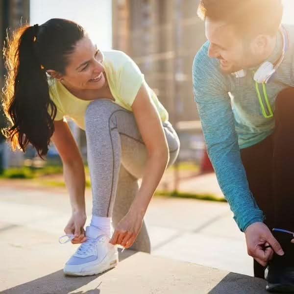 Ein Mann und eine Frau binden sich die Schnürsenkel ihrer Sportschuhe, bereit für das Training.