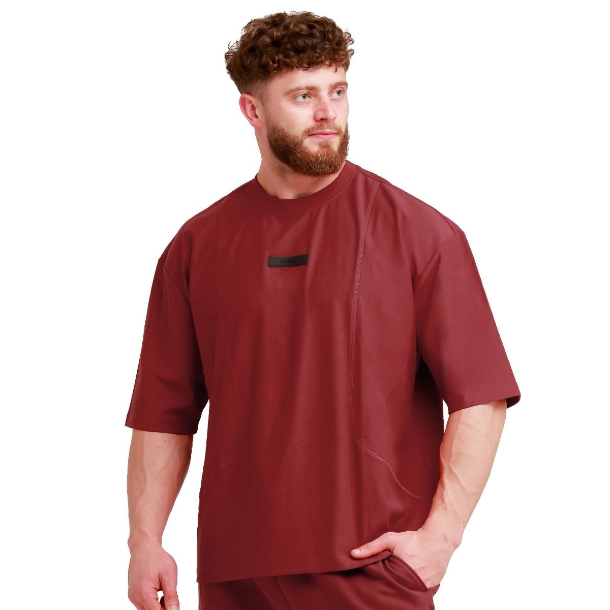 Nahaufnahme eines Mannes in einem roten Oversize T-Shirt mit kurzen Ärmeln und einem Brust-Logo-Patch.
