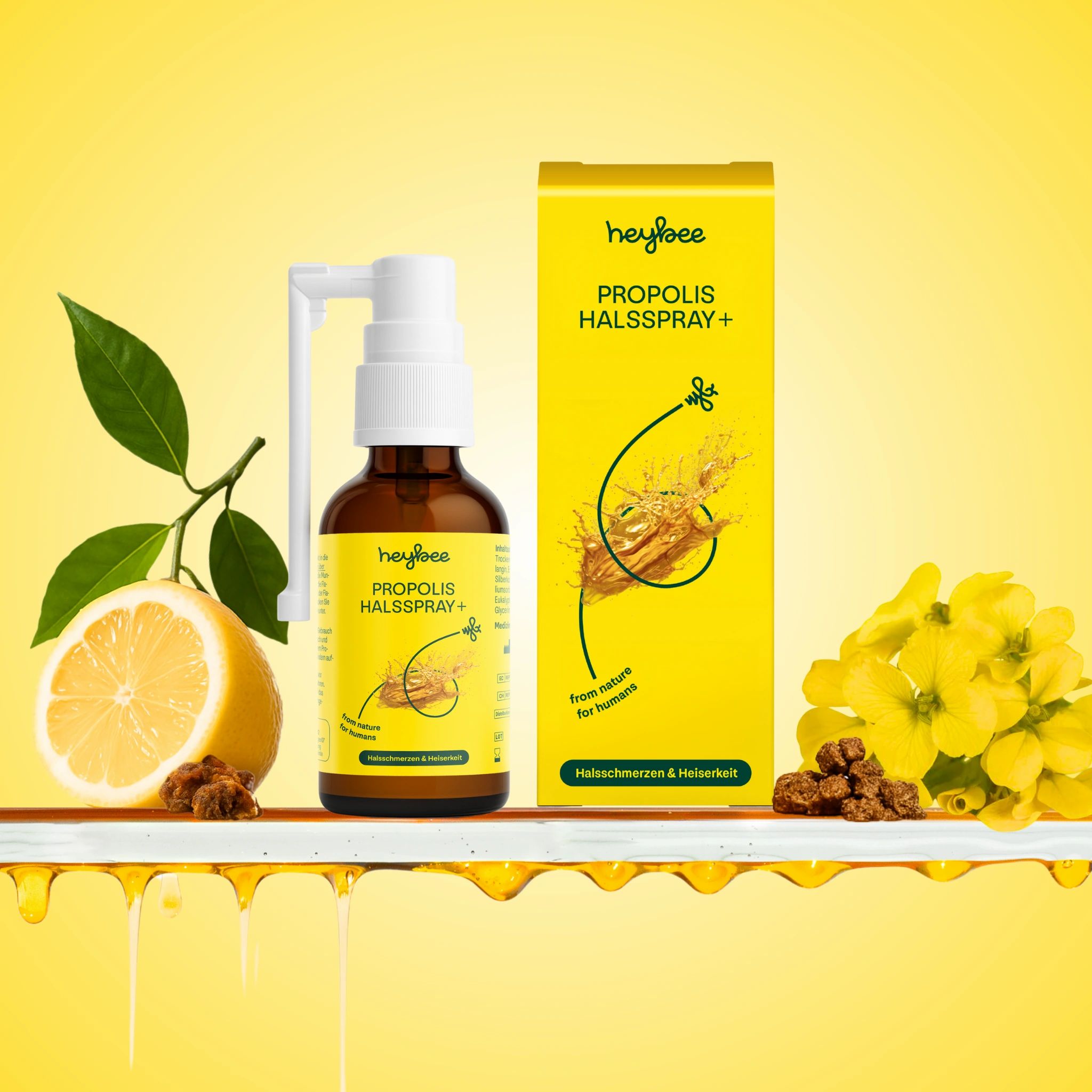 Heybee Propolis Halsspray+ Flasche und Verpackung mit Zitrone, Blüten und Propolis. Gelber Hintergrund.