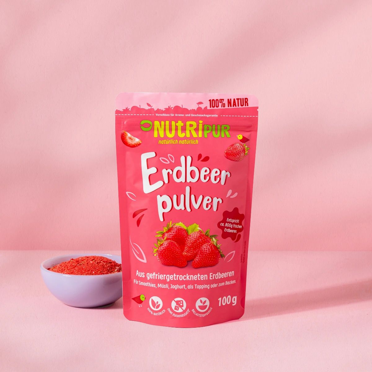 Rosa Beutel mit Erdbeerpulver. Aufschrift: NutriPur, Erdbeerpulver, 100% Natur. Eine Schale mit Pulver daneben.