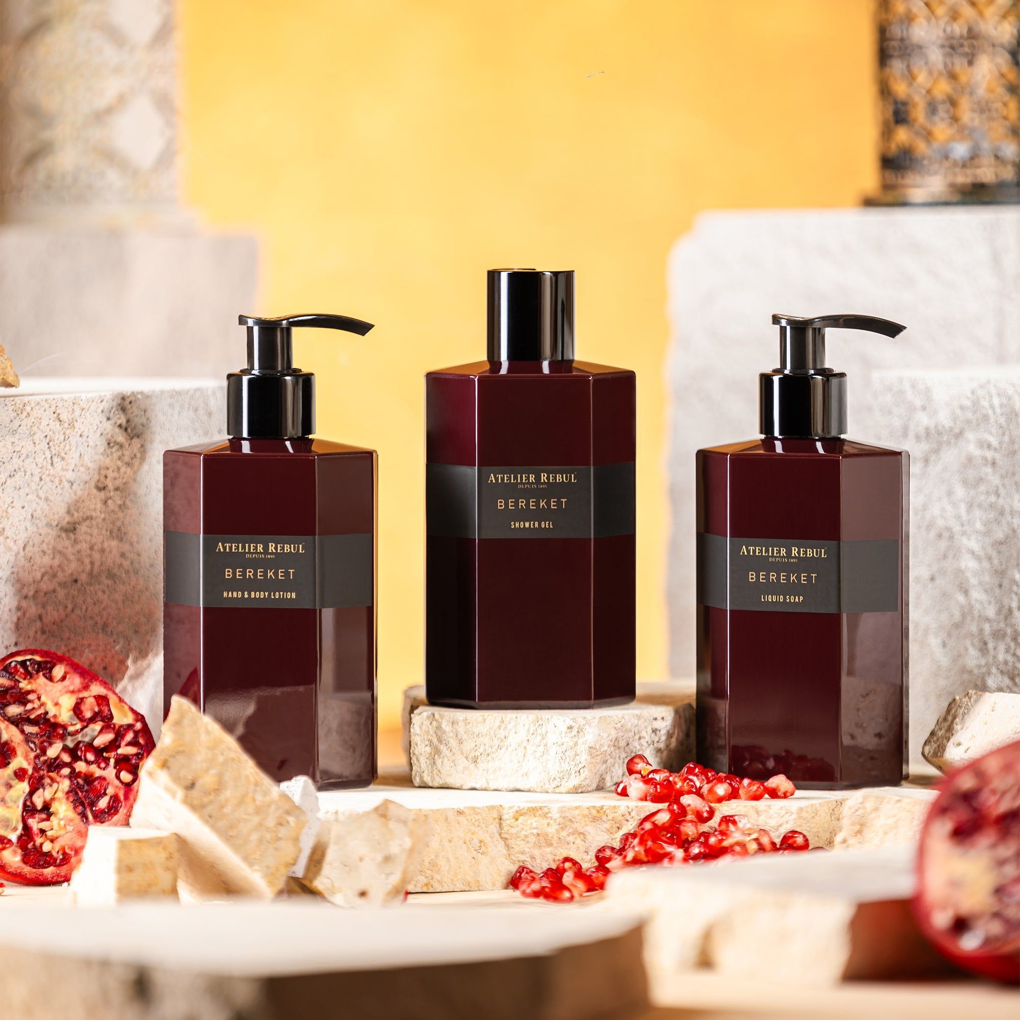 Drei Flaschen Atelier Rebul Bereket. Eine Duschgel, zwei mit Pumpaufsatz. Aufschrift: Atelier Rebul Bereket. Auf Steinen platziert.