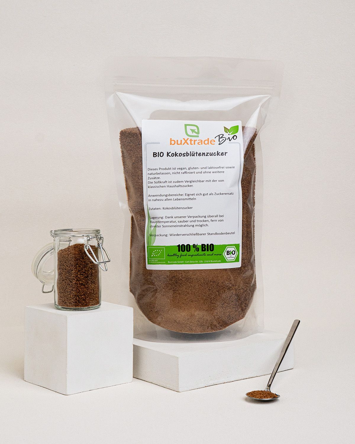 Verpackung und Glasbehälter mit braunem Zucker. Löffel daneben. Aufdruck: BIO Kokosblütenzucker, 100% BIO.