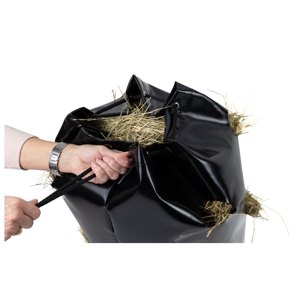 Person zieht Kordelzug eines schwarzen Heusacks. Der Sack ist mit Heu gefüllt.