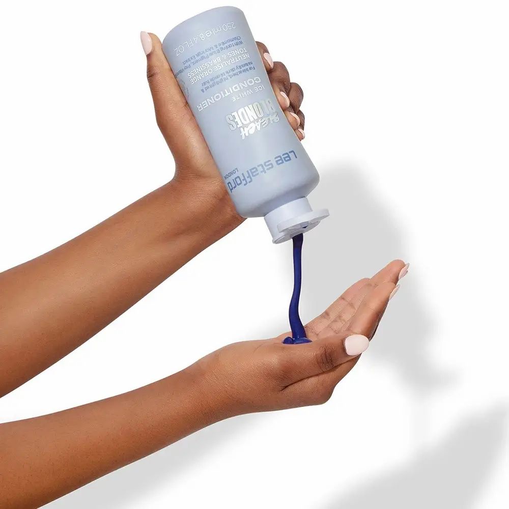 Eine Hand hält eine Lee Stafford Bleach Blondes Conditioner Flasche, während das Produkt in die andere Hand gegossen wird.