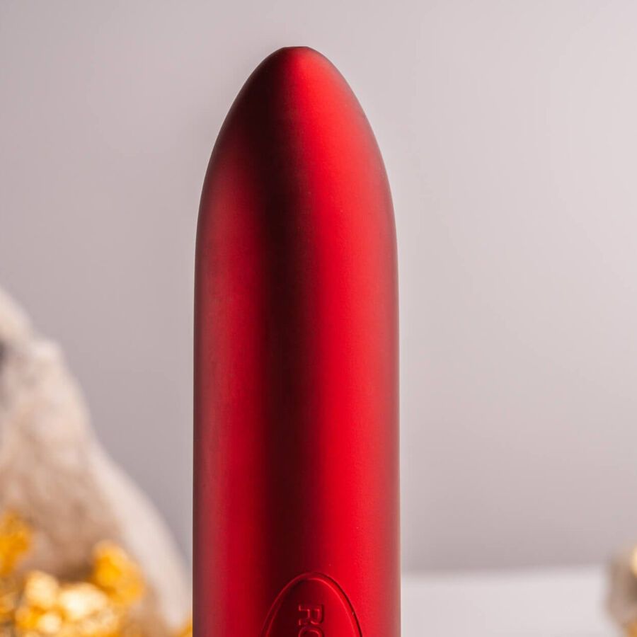 Roter Vibrator, zylindrisch, abgerundete Spitze. Auf weißem Hintergrund, neben Stein und Gold.