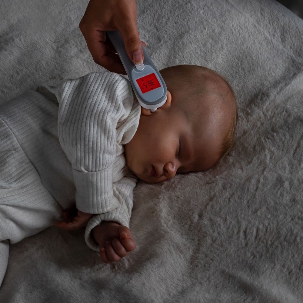 Ohrthermometer wird am Ohr eines Babys gehalten. Rote Temperaturanzeige auf dem Display.