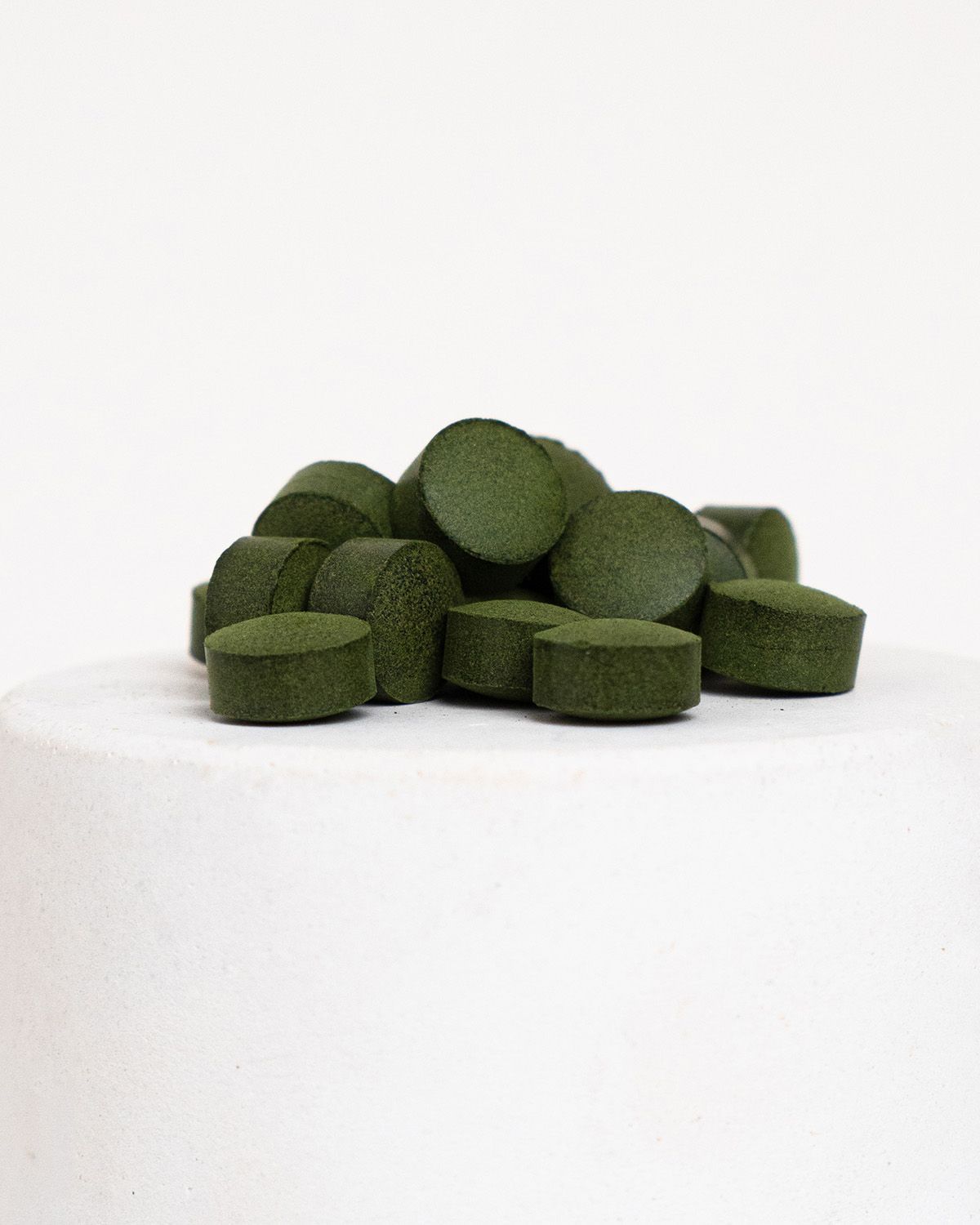 Haufen grüner Chlorella Tabs auf einem weißen Podest. Runde Form, flache Oberfläche.