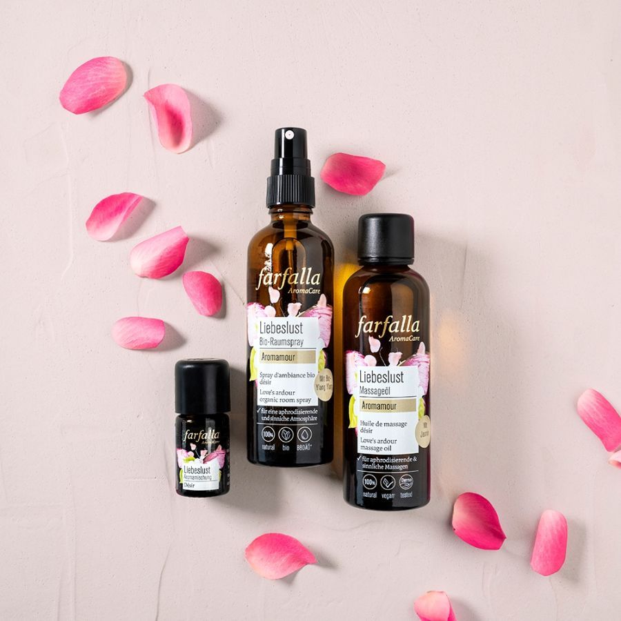 Drei braune Glasflaschen von Farfalla Aromamour. Etiketten mit Text. Rosenblütenblätter liegen verstreut.