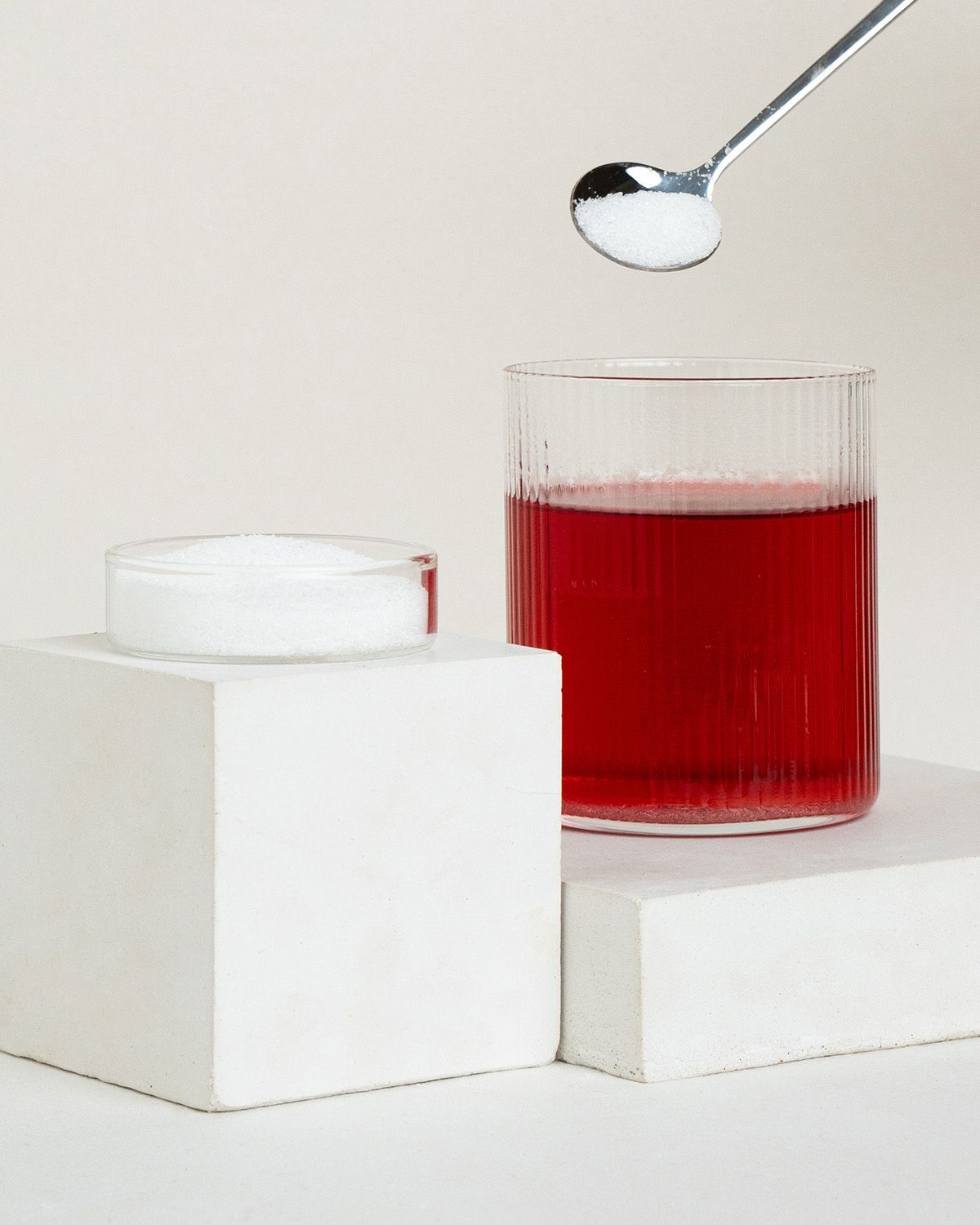 Ein Glas rotes Getränk, ein Löffel Erythritol und eine Schale mit Erythritol.