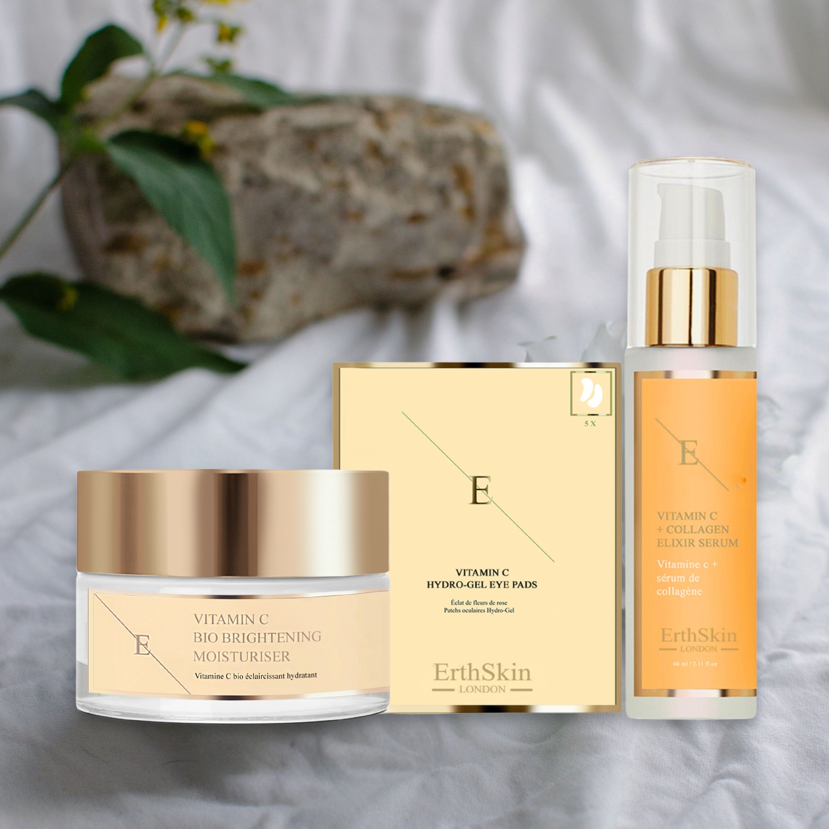 ErthSkin-Produkte: Vitamin C Elixier Serum, Bio Brightening Moisturizer und Augenpads. Auf weißem Stoff. Produkte nebeneinander.