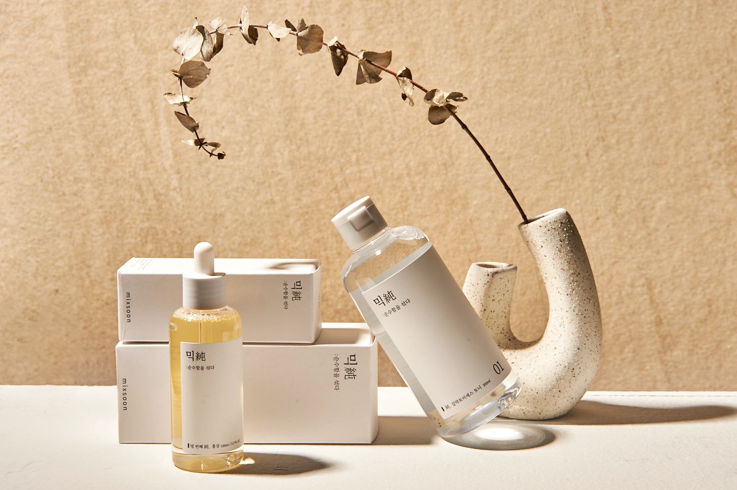 Mehrere Flaschen und Kartons. Eine Flasche mit Sprühkopf. Beige Hintergrund. Dekorative Vase mit Zweig.