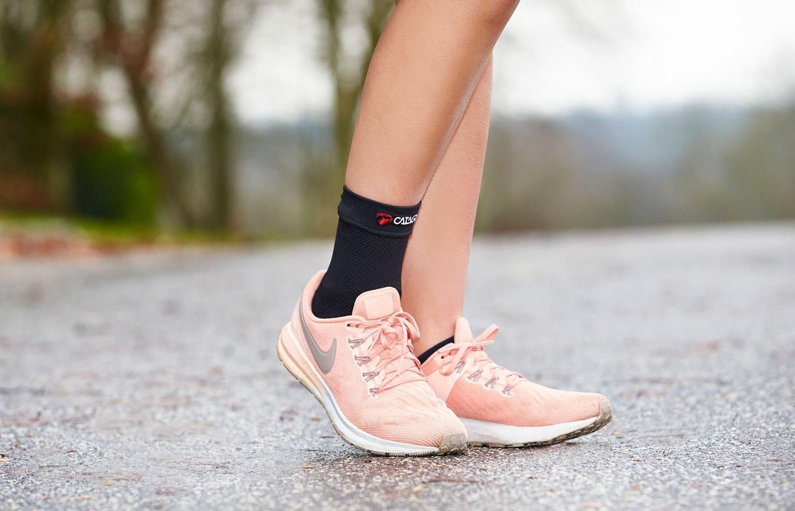 Schwarze CATAGO Knöchelbandage FIR-Tech Healing am Bein. Trägt Sportschuhe. Logo sichtbar.