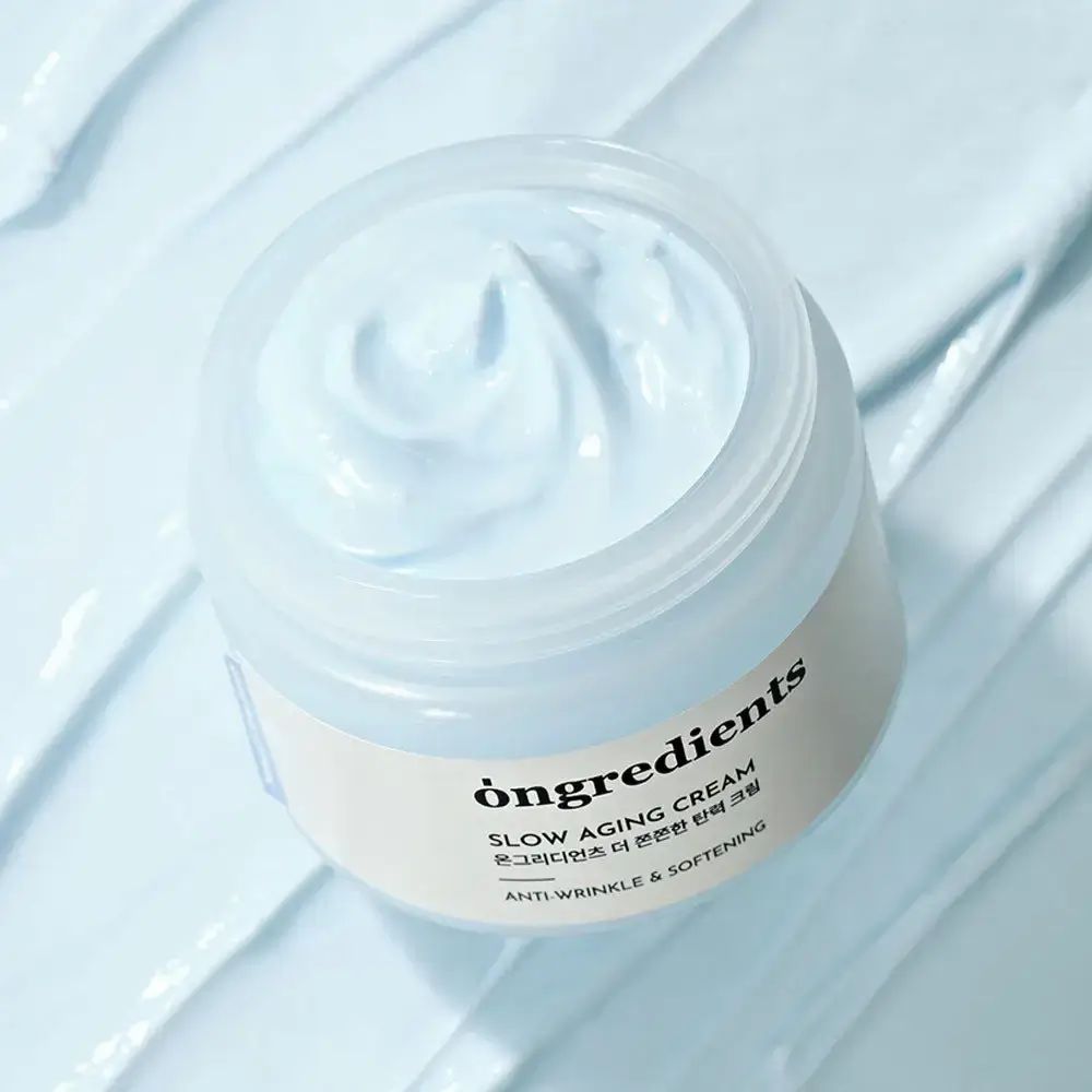 Offenes Creme-Glas mit Creme. Aufschrift: Ongredients, Slow Aging Cream, Anti-Wrinkle & Softening.