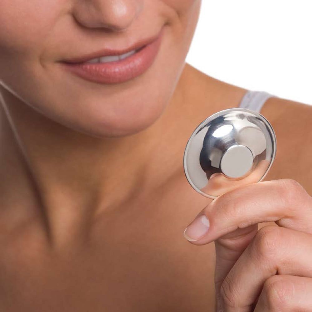 Nahaufnahme: Frau hält einen silbernen Brustwarzen Schütz. Runde Form, leicht gewölbt.