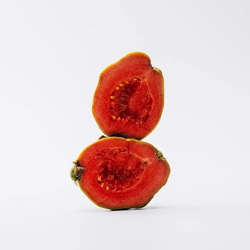 Zwei Hälften einer Guave, aufgeschnitten. Rotes Fruchtfleisch mit kleinen Kernen. Grüne Schale. Auf weißem Hintergrund.